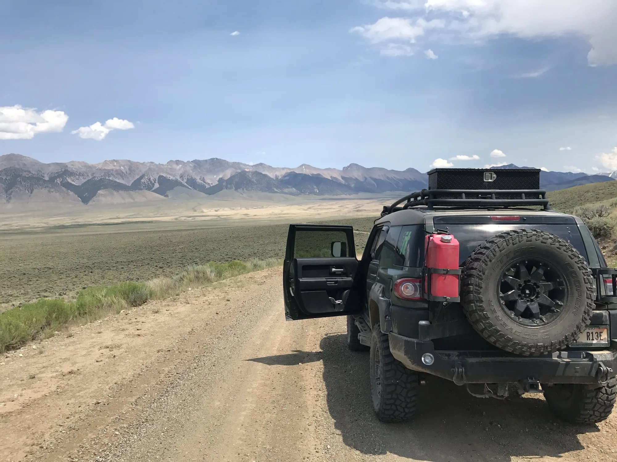 A black off-road truck on a gravel road across open sagebrush plains, mountains on the horizon